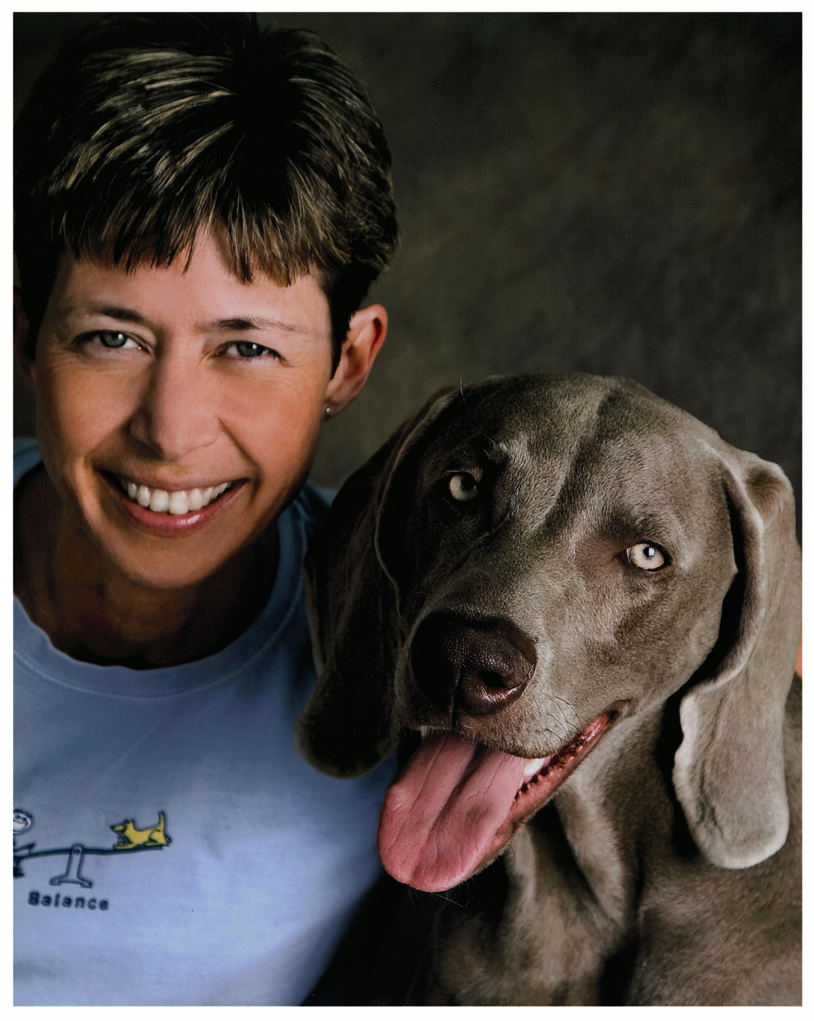 Woman with short brown hair smiling towards camera with grey weimaraner dog
