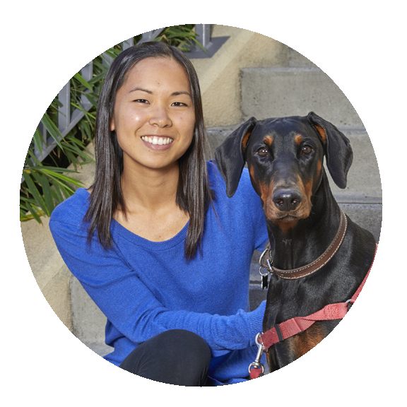 Woman with long dark hair facing the camera smiling with a doberman beside her facing camera