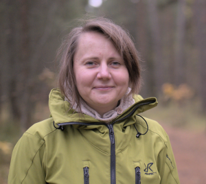 Woman with shoulder length brown hair smiling and facing the camera.  She is wearing a green jacket.