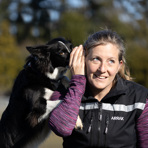 Christina Young smiling looking slightly right while border collie dog appears to whisper in her ear