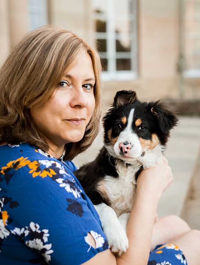 Simone Mueller facing camera wearing a blue dress and holding a puppy