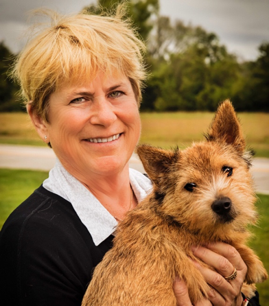 Woman with short blond hair smiling facing camera holding a border terrier