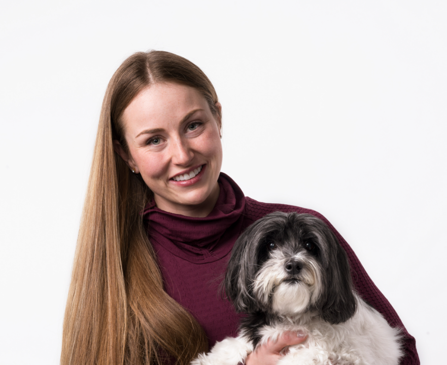 Woman with straight long brown hair smiling facing camera holding small black and white dog