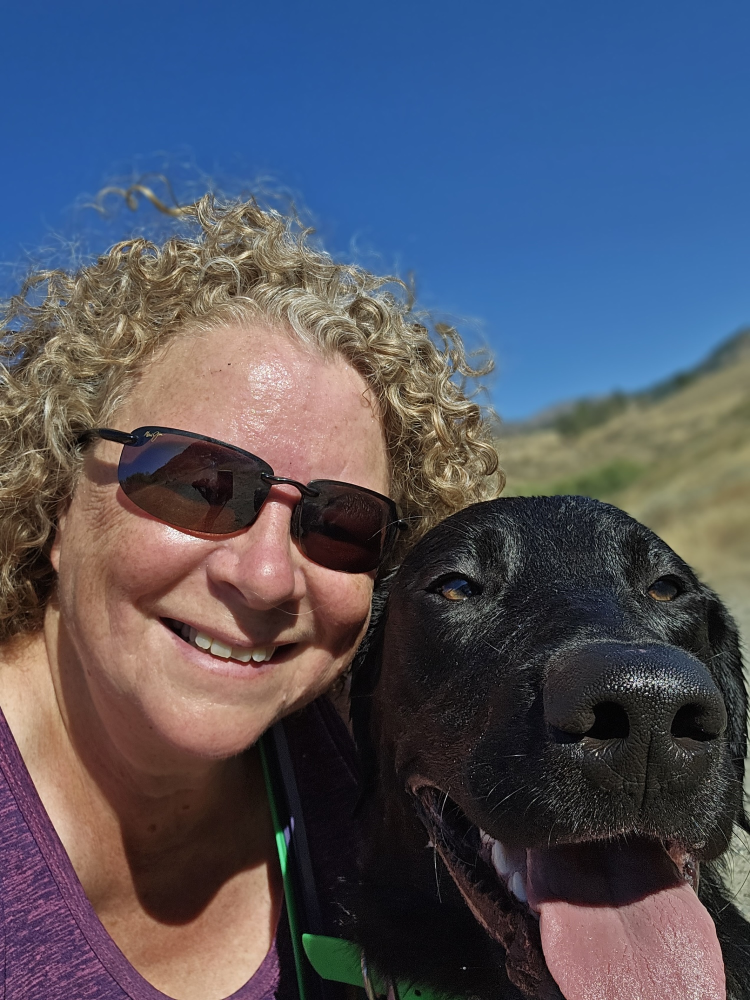 Teri Martin smiling facing camera with black labrador Maverick